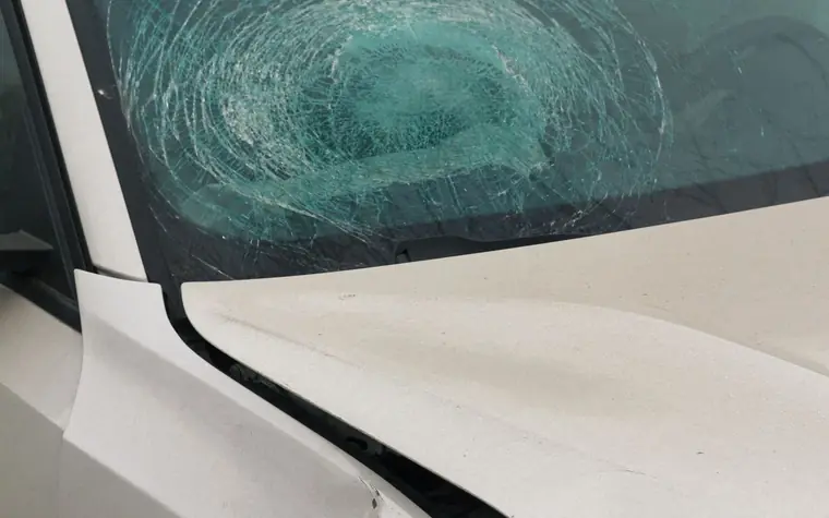 Unfallschaden: gesplitterte Windschutzscheibe und beschädigte Front an einem weißen Pkw