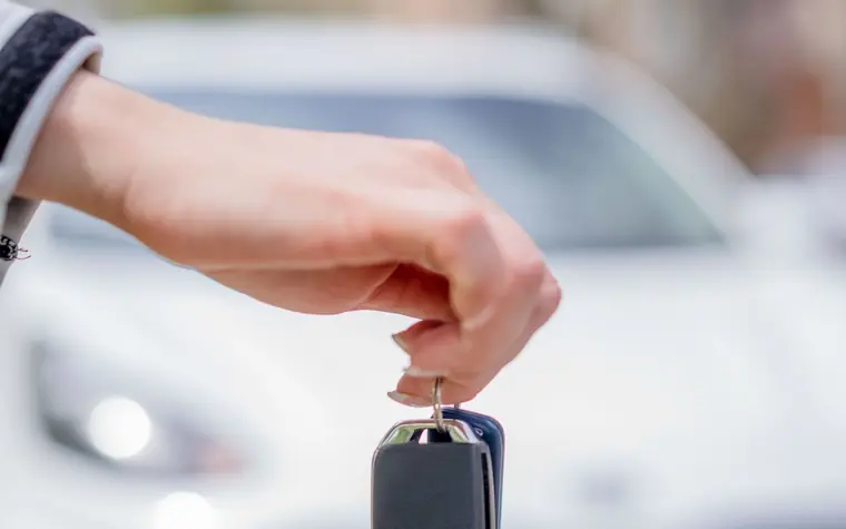 Fahrzeugbewertung: Hand hält Autoschlüssel, im Hintergrund ein weißes Auto